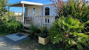 Uma casa térrea com varanda coberta, um pequeno deck e um jardim com diversas plantas.