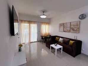 A living room with a sofa, a coffee table, a TV mounted on the wall, and a ceiling fan. - Cozy 1-bedroom apartment in charming Boca Chica with AC (Boca Chica)