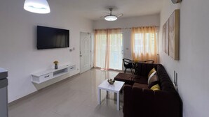 Ein Wohnzimmer mit Flachbildfernseher, Deckenventilator, Essbereich mit Tisch und Stühlen sowie einer Couch.