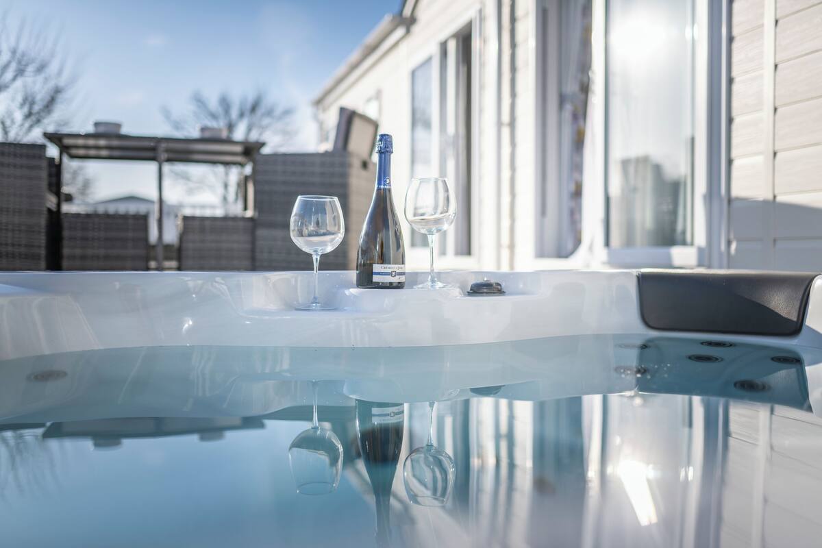 A hot tub with two glasses and a bottle, a clear glass surface, and a building in the background.