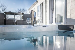 Un jacuzzi con dos vasos y una botella, una superficie de vidrio transparente y un edificio al fondo.