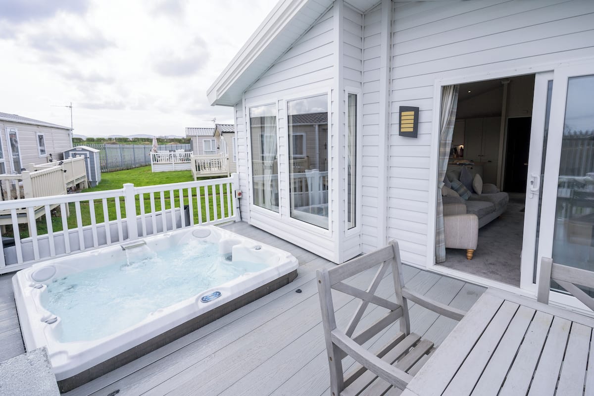 A deck with a hot tub, a covered patio, and a sliding glass door leading to a living area.