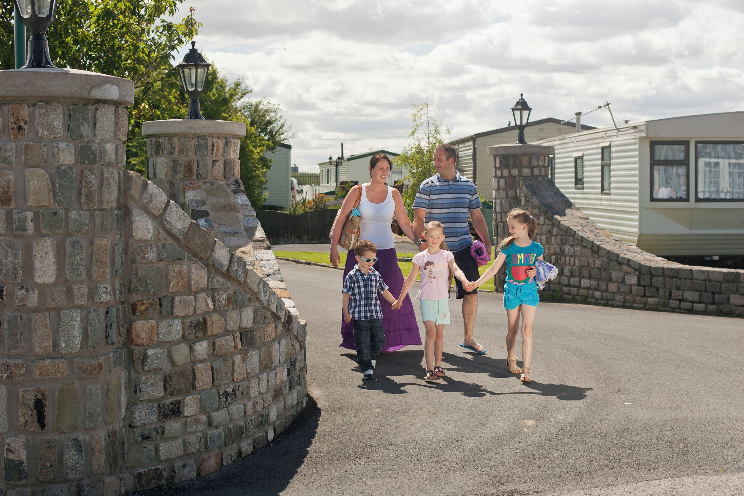 A family walking on a paved path with stone walls and a lamp post.
