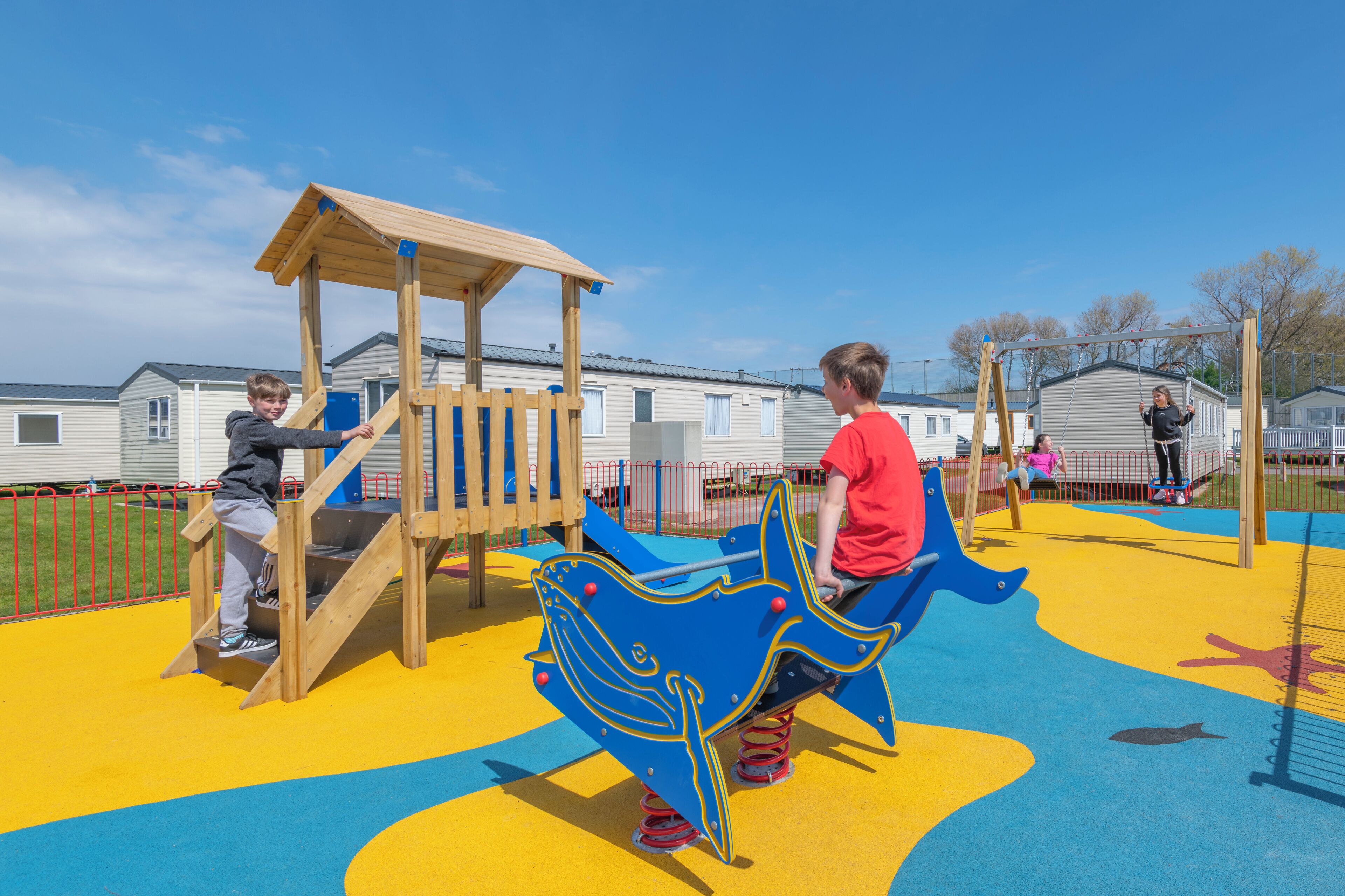 Ein Spielplatz mit einer hölzernen Kletterkonstruktion und einem blau-gelben Spielbereich.