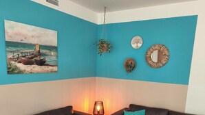 Ein Wohnzimmer mit zwei schwarzen Sofas, einem Holztisch, einem Gemälde mit Küstenlandschaft und einer Deckenleuchte.