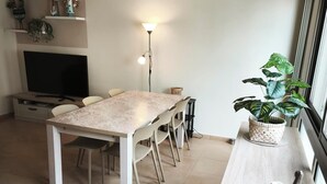 Ein Essbereich mit Tisch, Stühlen, Fernseher, Lampe und Pflanze.