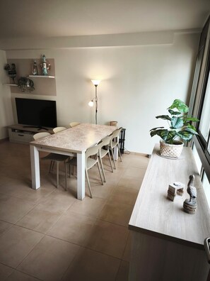 Een eethoek met een tafel, stoelen, een televisie, een lamp en een plant.