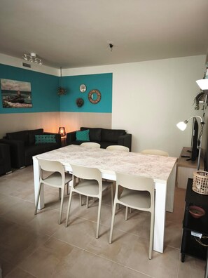 Een zithoek met een tafel en stoelen, een bank, een muur met decoratieve objecten en een plafondlamp.
