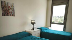 Ein Zimmer mit zwei Betten, einem Nachttisch mit Lampe, einem Bild an der Wand und einem Fenster mit Aussicht.