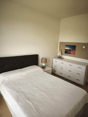 Een slaapkamer met een groot bed, een nachtkastje met een lamp, een dressoir en een aan de muur hangend schilderij.
