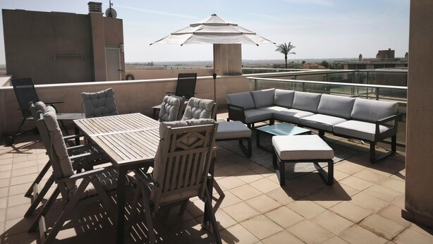 Eine Dachterrasse mit Esstisch, Stühlen, einer Couch und einem Sonnenschirm.
