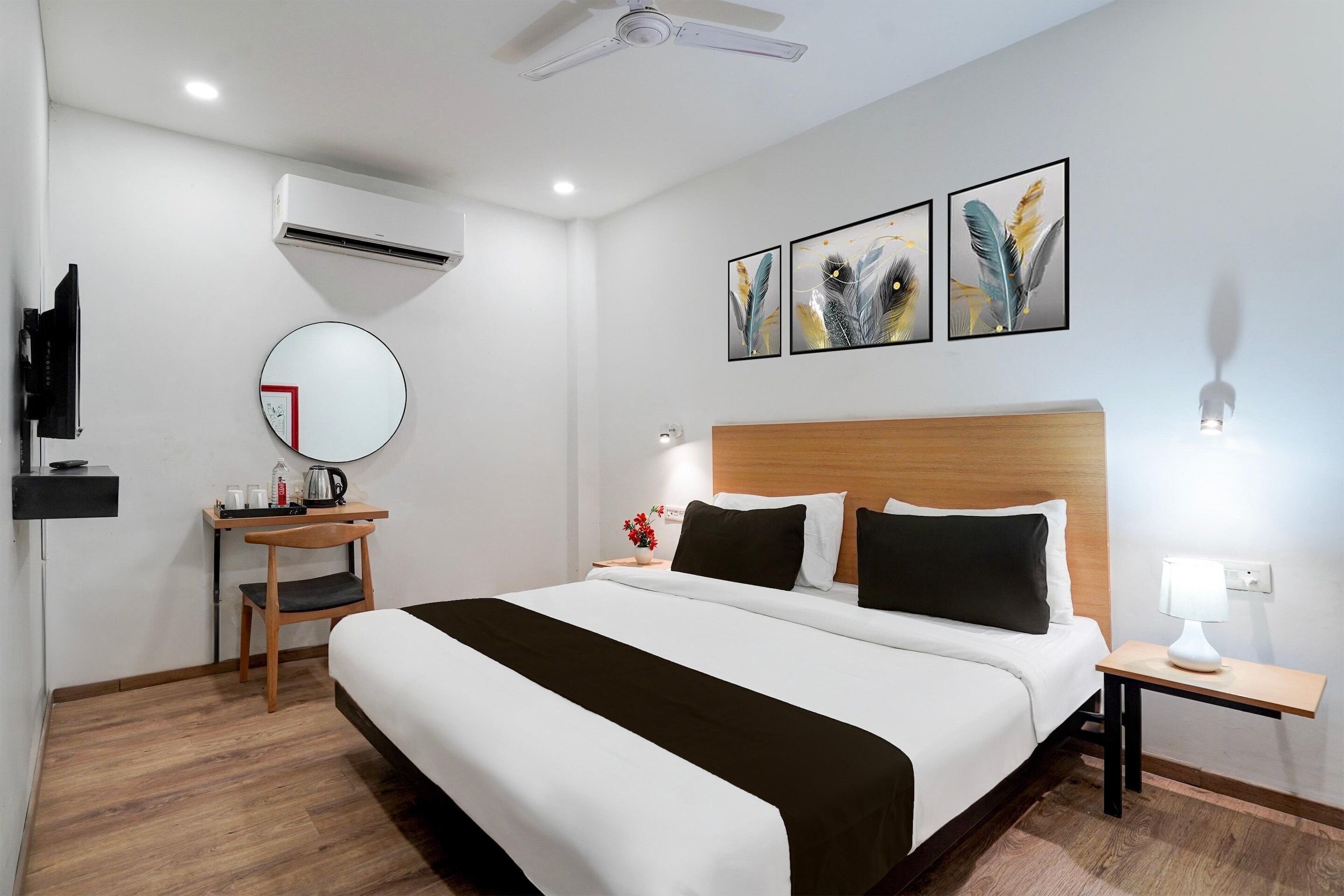 A hotel room with a bed, bedside table, lamp, wall-mounted air conditioner, mirror, and artwork.