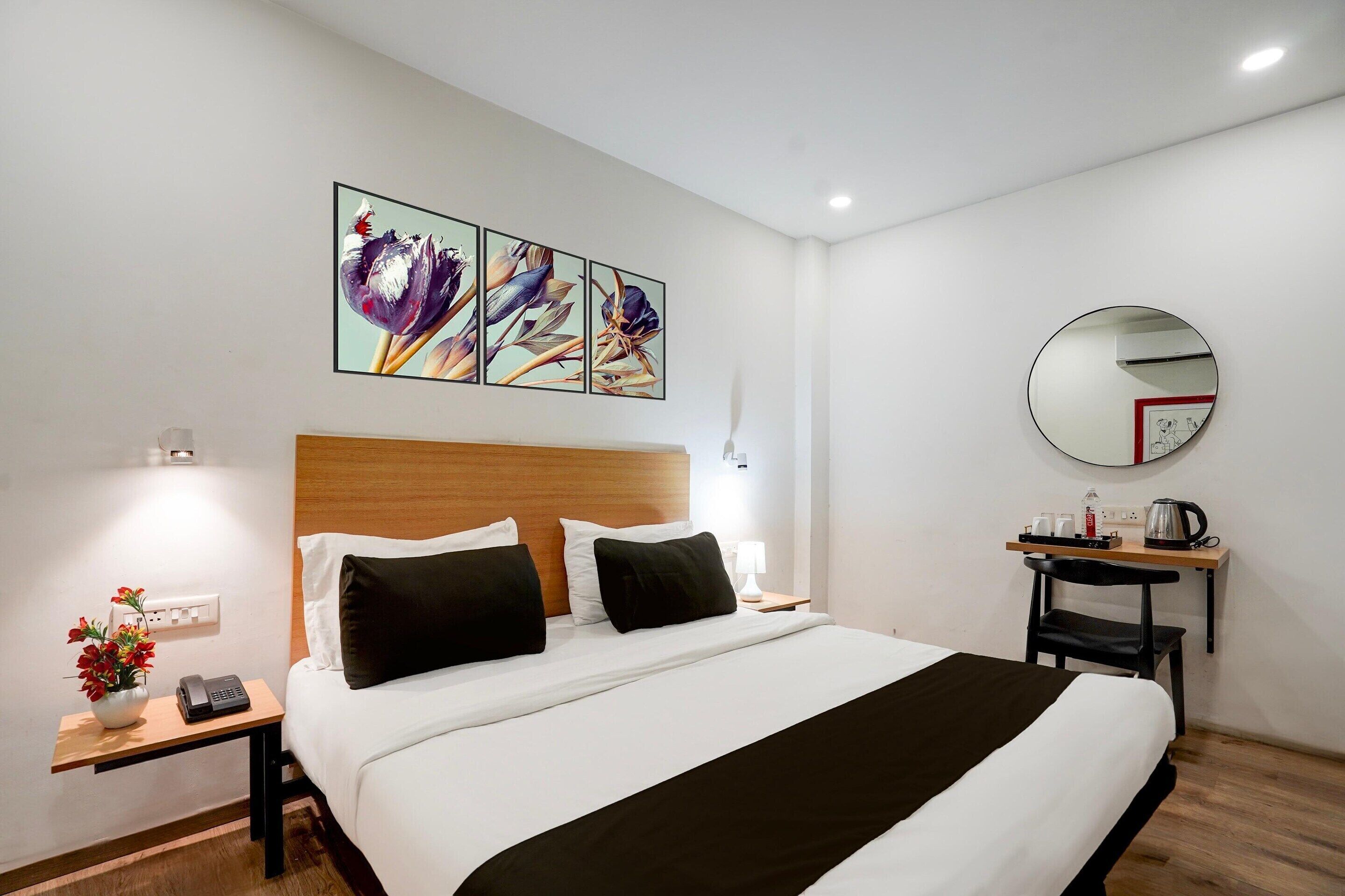 Ein Hotelzimmer mit Bett, Nachttisch, Lampe, Kunstwerk und einem runden Spiegel.