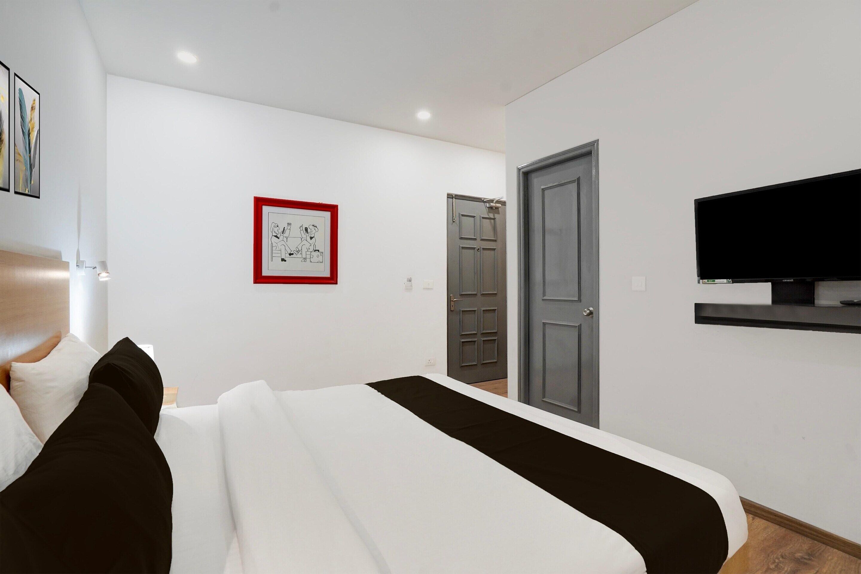 Une chambre à coucher avec un lit, une télévision, une porte et un tableau encadré au mur.