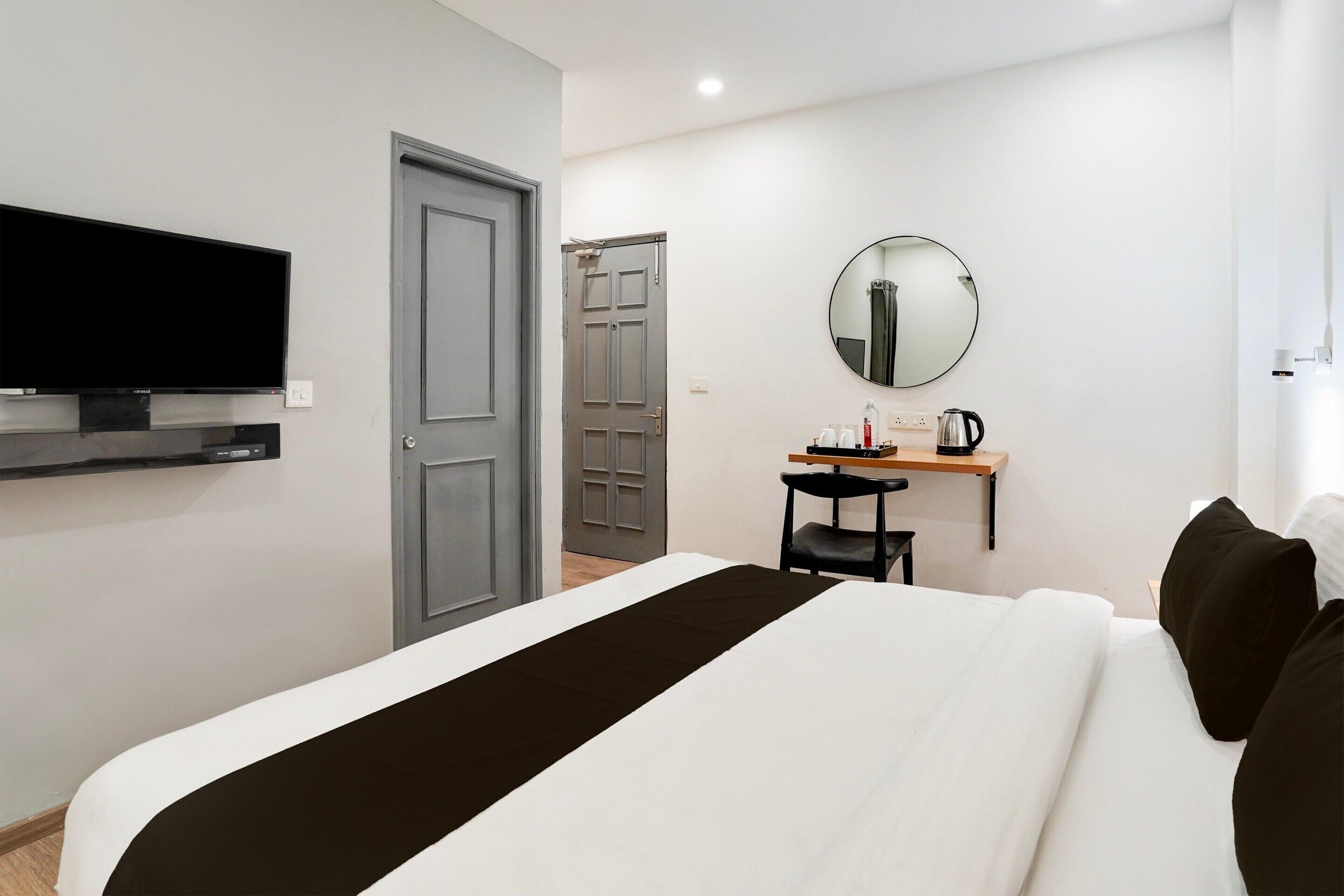 Una habitación de hotel con cama, un escritorio con silla, televisor montado en la pared y una puerta.