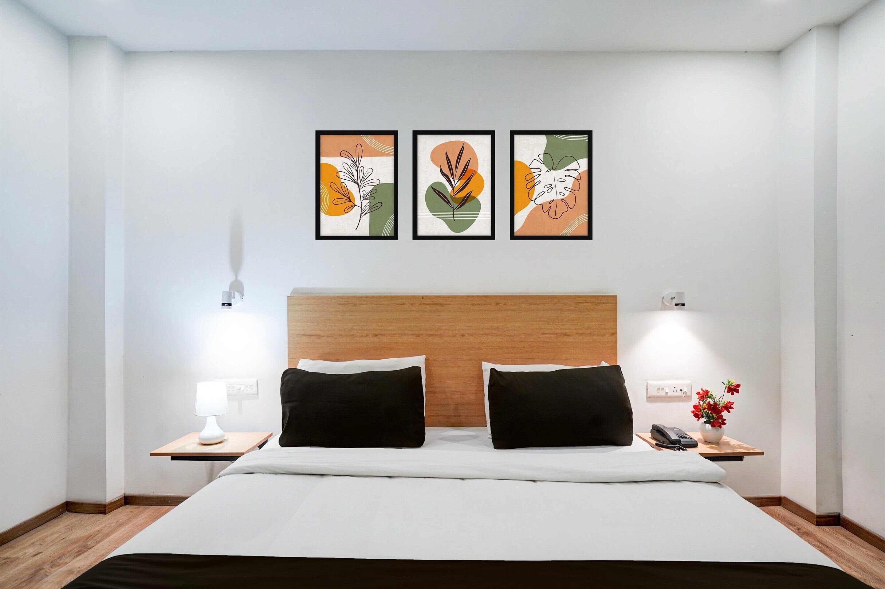A hotel room with a bed, two black pillows, a nightstand with a lamp, a phone, and a small table with a vase of flowers.