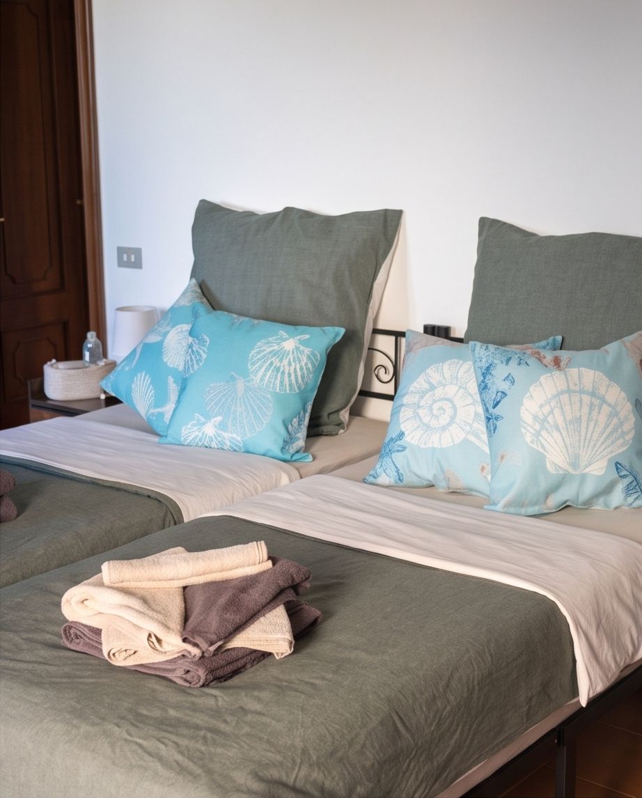 A double bed with two pillows, a folded towel, and a bedside table with a lamp.