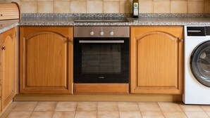 Una cocina con armarios de madera, estufa, horno, lavadora y salpicadero de azulejos.