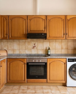 Eine Küche mit Holzschränken, einem Herd, einem Backofen, einer Waschmaschine und einer gefliesten Spritzschutzwand.