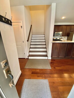 Una escalera conduce a una zona de cocina con suelo de madera y un microondas.
