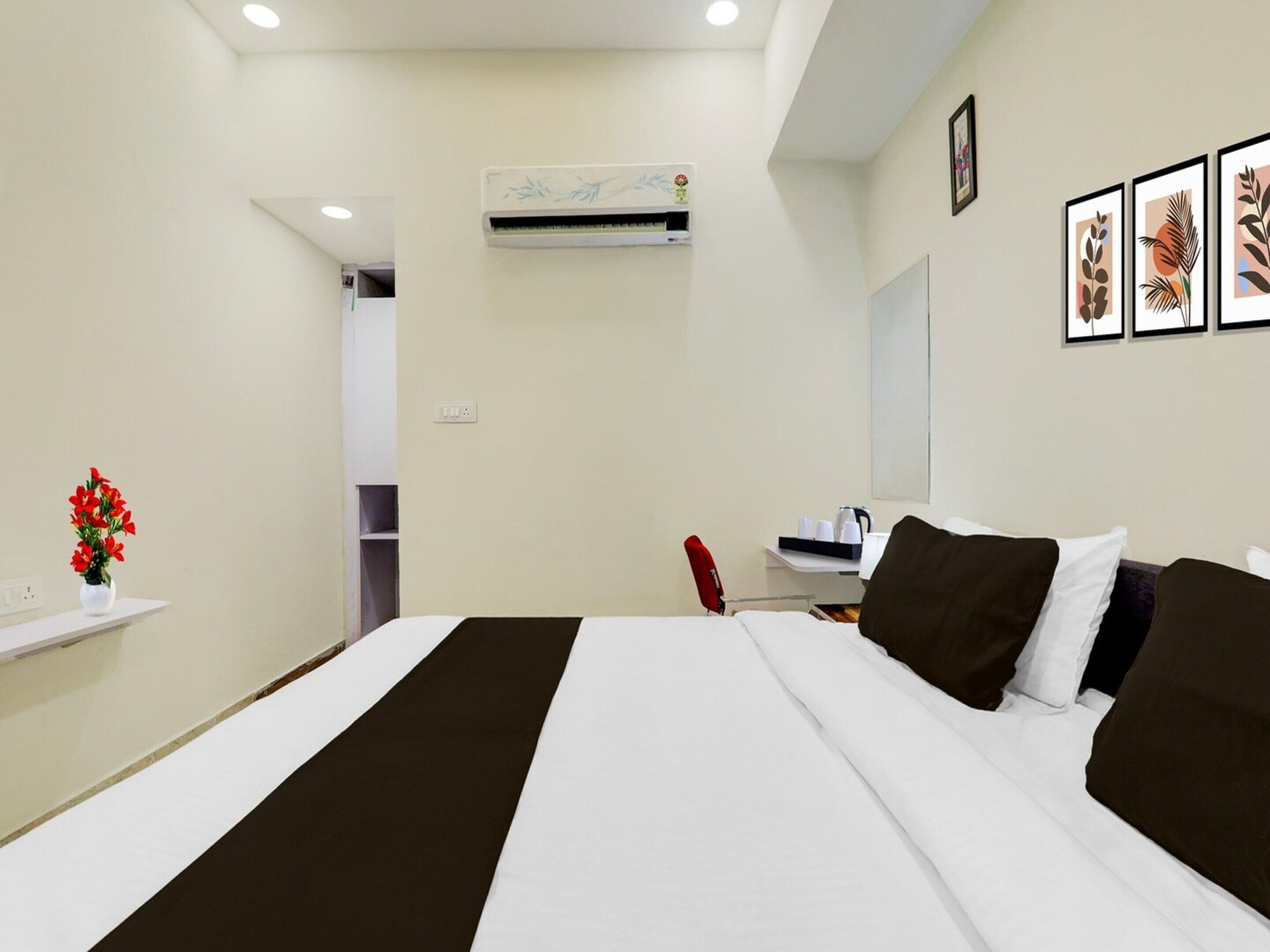 A hotel room with a bed, a desk, a chair, an air conditioning unit, and a wall with framed pictures.