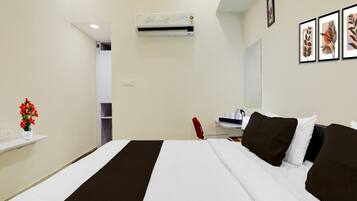 A hotel room with a bed, a desk, a chair, an air conditioning unit, and a wall with framed pictures.