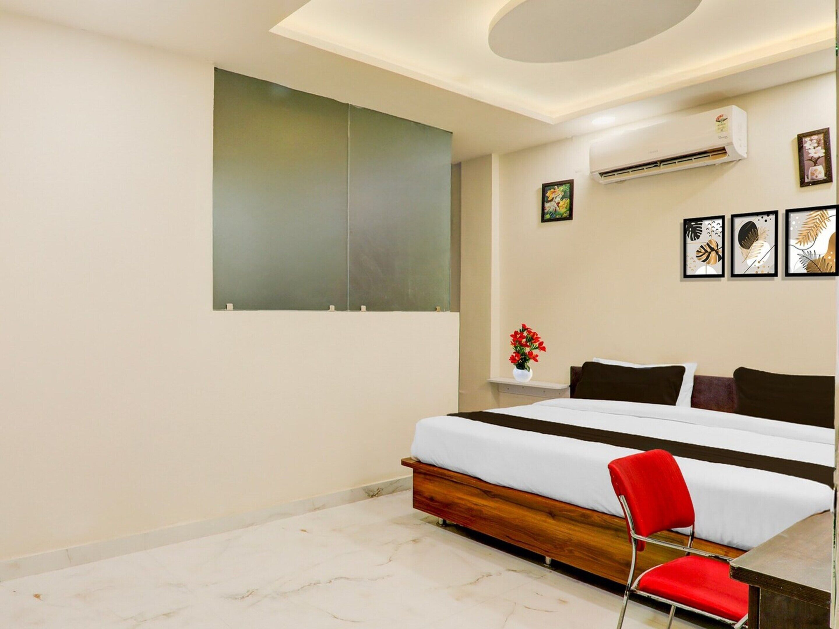 A modern bedroom with a bed, a red chair, a wall-mounted air conditioner, and framed artwork.
