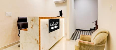 A reception desk with a sign reading 'Collection,' a leather chair, and a staircase in the background.