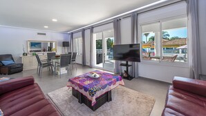 Un salón espacioso con comedor, televisor de pantalla plana y ventanas amplias con vistas al exterior.