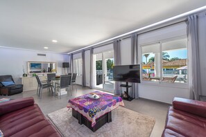 A spacious living room with a dining area, a flat-screen TV, and large windows offering a view of the outdoors. - Villa with a private heated pool, 4 bedrooms, 4 bathrooms, 10 minutes from the beach (Marbella)