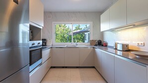 Una cocina moderna con electrodomésticos de acero inoxidable, armarios blancos y una ventana con vistas a zonas verdes.