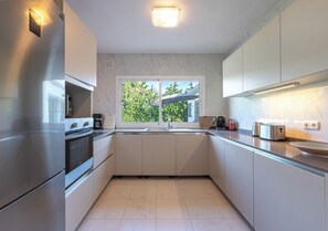 A modern kitchen with stainless steel appliances, white cabinetry, and a window providing a view of greenery. - Villa with a private heated pool, 4 bedrooms, 4 bathrooms, 10 minutes from the beach (Marbella)