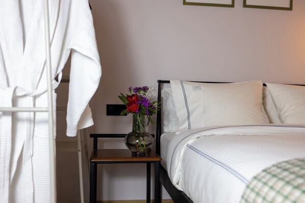 A bedroom with a bed, a bedside table, a vase with flowers, and a white robe hanging on a rack.