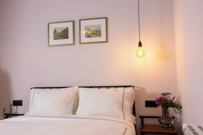 A neatly made bed with white linens, a bedside table with a vase of flowers, and two framed pictures on the wall.