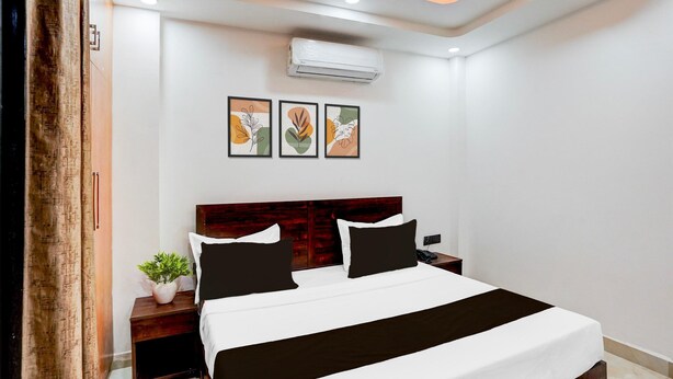 A hotel room with a bed, a nightstand, a potted plant, and three framed artworks on the wall. - Cosy Stays at Sector 143b Noida (Noida)