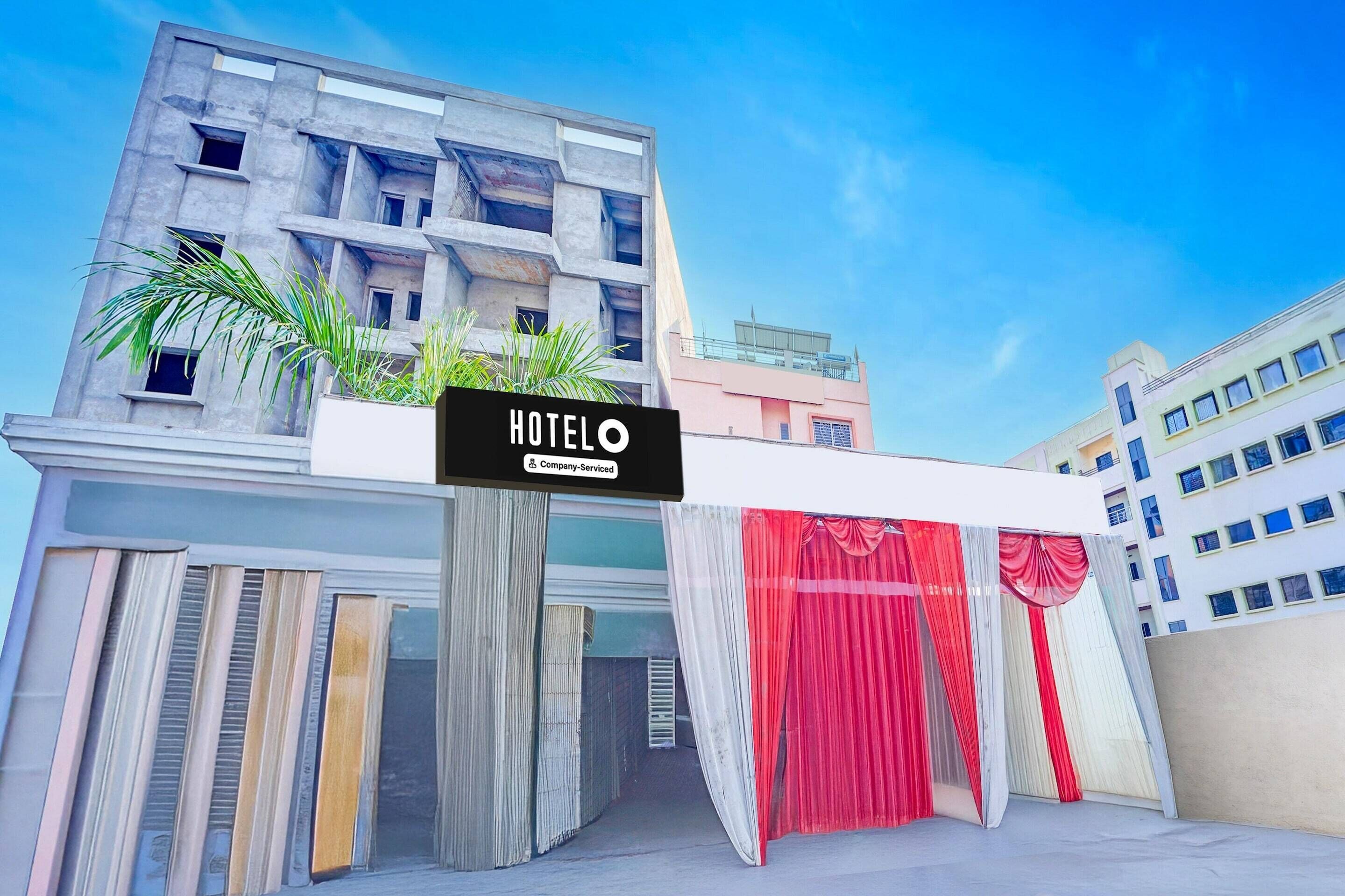 Un hôtel avec une enseigne, une façade moderne et une entrée surmontée d’un rideau rouge.