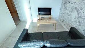 En stue med en sort lædersofa, et træsofabord og et fjernsyn på et stativ.