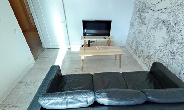 Un soggiorno con un divano in pelle nera, un tavolino in legno e una televisione su un mobile.