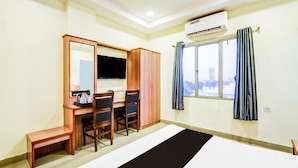 Une chambre d’hôtel comprenant un lit, un bureau avec des chaises, une télévision, un appareil de climatisation et une fenêtre avec des rideaux.