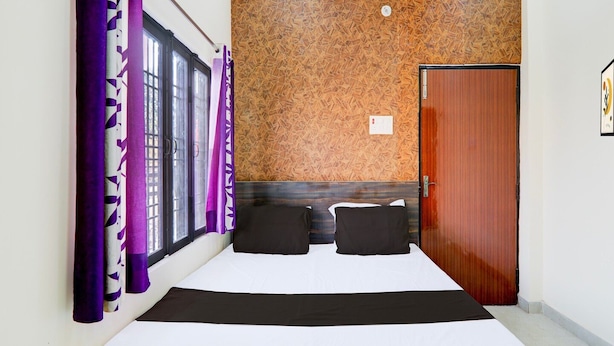 A bedroom with a bed, a window with purple curtains, a wooden headboard, and a door. - Saver Doublesuper Hotel O Sudhirpur (Varanasi)