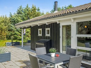 En modern uteplats med ett matbord och stolar, en grill och ett stort fönster.