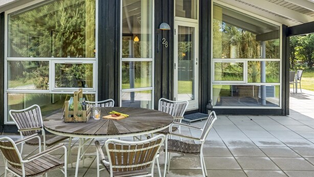 A covered patio with a round table and chairs, large windows, and a door marked with the number 28. - "Ilya" - 900m from the sea by Interhome (Løkken)