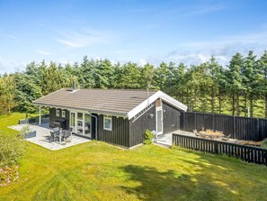 Ett modernt hus med en uteplats, en täckt sittgrupp utomhus och en inhägnad trädgård.
