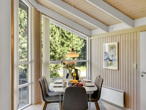 Comedor con mesa dispuesta para dos, ventanas amplias, lámpara colgante y radiador.