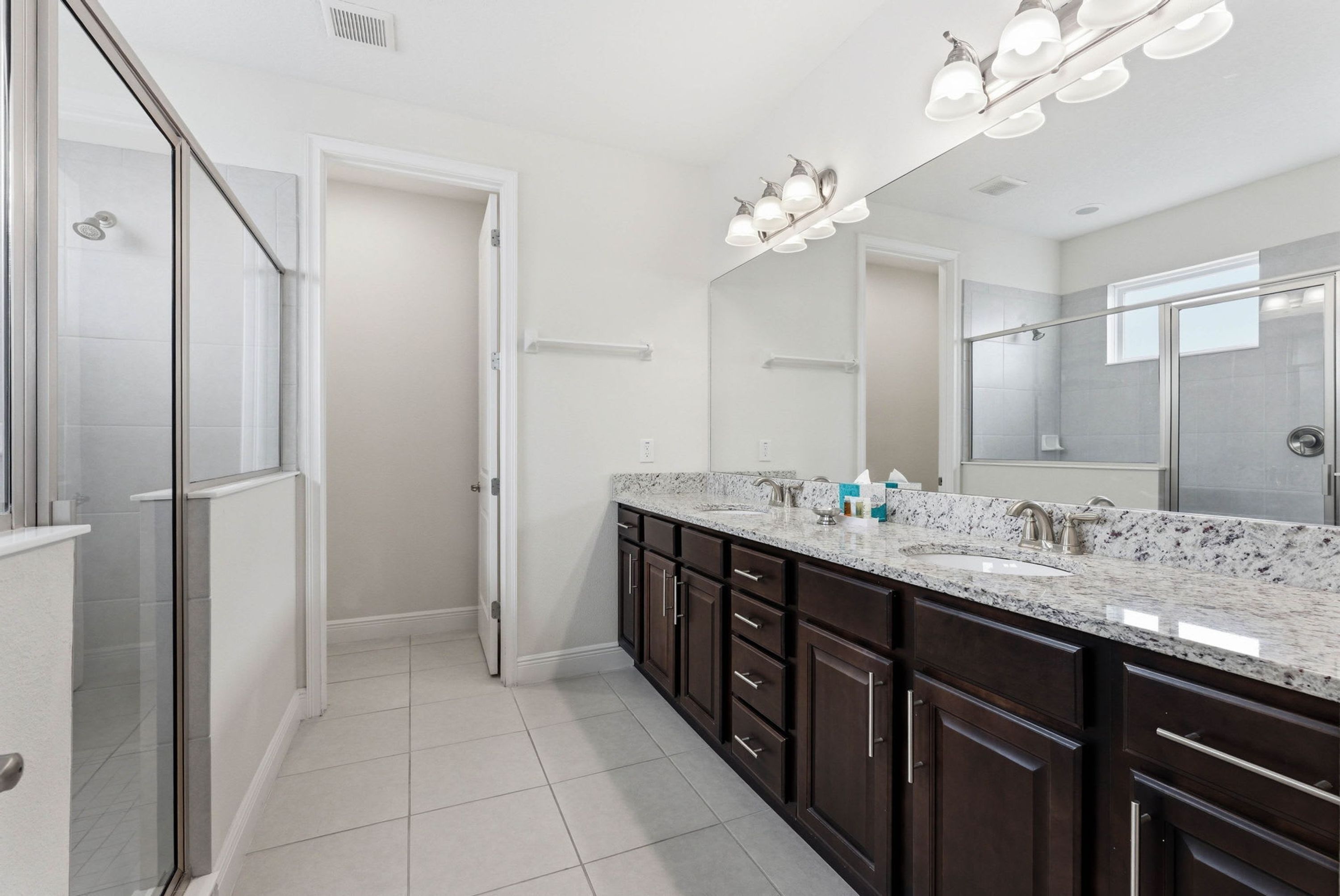 A modern bathroom with a glass shower enclosure, dark wooden cabinets, a granite countertop, and a large mirror.