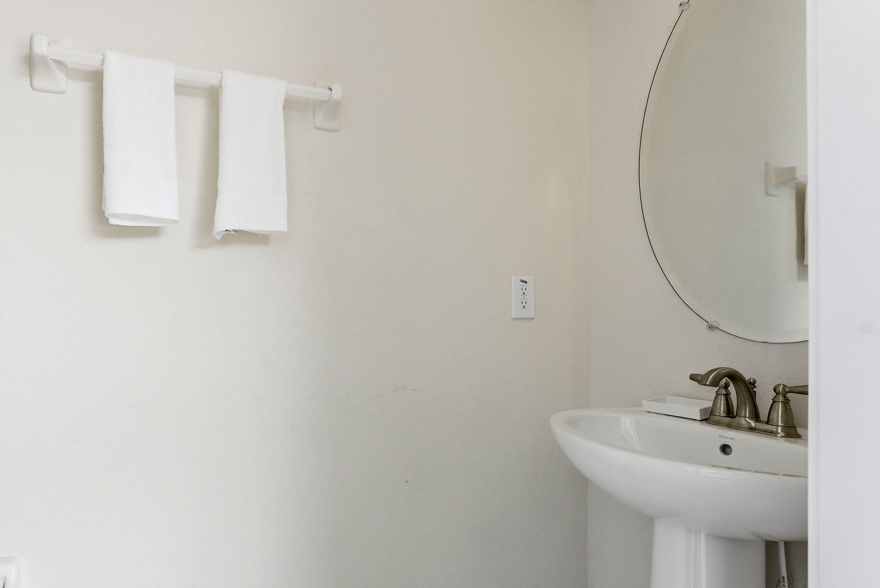 Une salle de bain avec un lavabo blanc, un miroir et deux serviettes blanches suspendues à un porte-serviettes.