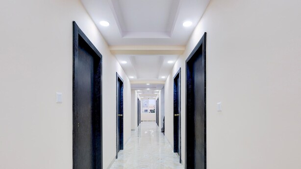 Un pasillo largo y estrecho con puertas a ambos lados, iluminación empotrada y suelo de baldosas.