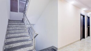 Una escalera con barandillas de metal, un pasillo con piso de mármol y puertas a la derecha.