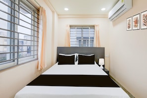 Une chambre d’hôtel avec un lit, une table de chevet, un climatiseur et une fenêtre avec des rideaux.