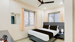 Un dormitorio con cama, mesita de noche, lámpara, ventilador de techo y ventanas con cortinas.